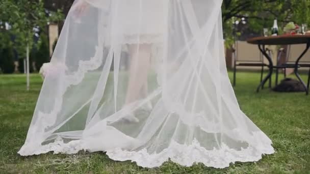 Close-up young bride full length back view wearing long lace, white wedding dress and bridal veil which walks in his green yard at private home — Stock Video