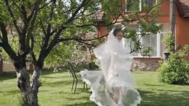 Güzel gelin etrafında döner, gülümsüyor ve bahar bahçe evinin yakınındaki bir güneşli sabah yürür uzun bir dantel ile beyaz bir elbise içinde. Sabah gelin