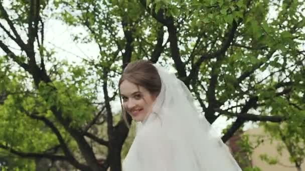 Detail modelu nevěsty, který se usmívá do kamery a nosí bílé šaty dlouhé krajkové. Mladá dívka chodí v zelené zahradě. Svatební den
