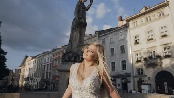 Hermosa joven rubia con el pelo largo de pie al atardecer del este en el casco antiguo. Día soleado de la mañana de verano — Vídeos de Stock