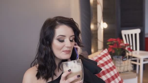 Közeli kép: egy gyönyörű fiatal barna lány egy csodálatos smink és frizura, hogy szórakoztató beszél a telefonon, és iszik forró kávé tejjel — Stock videók