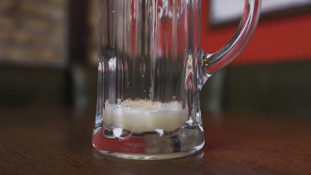 De cerca. Sobre la mesa hay un vaso vacío en el que se vierte cerveza con una espuma — Vídeo de stock