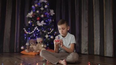 Adam Noel ağacı yakınındaki katta oturan ve kar küresi ile oynuyor. Noel akşam yeni yılı. Tatil ruh hali