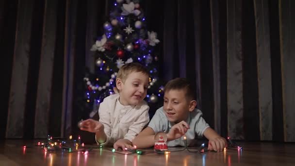 Δύο παιδιά αργά το βράδυ στο σπίτι Ξαπλώστε στο πάτωμα και να διασκεδάσουν παίζοντας με τα χρωματιστά φώτα που φωσφορίζουν. Έννοια των εορτών των Χριστουγέννων, Πρωτοχρονιάς, δώρα — Αρχείο Βίντεο