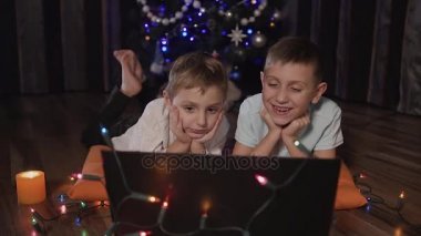 Küçük güzel çocuklar rahatlatıcı renkli garland ve mumlar çevrili katta yalınayak yalan bir Xmas ağacı önünde onu laptop ile bu akşam parıldıyor. Orta yol