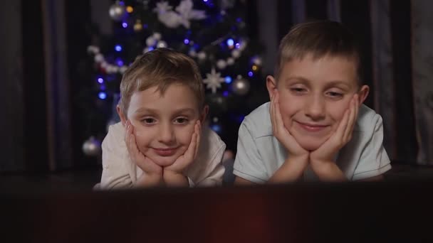 De cerca. Dos niños encantadores miran algo interesante en el portátil a través de Internet. Noche de Navidad, tiempo feliz, familia — Vídeo de stock