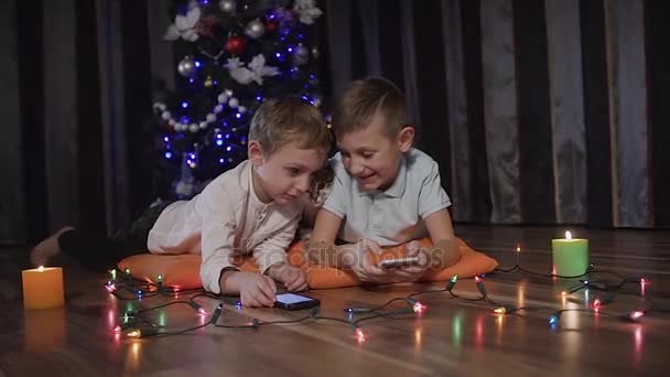 Dois meninos e seu gato jogando online e navegando na web com telefones em casa. Tempo de Natal, noite, ano novo, tecnologia, internet — Vídeo de Stock