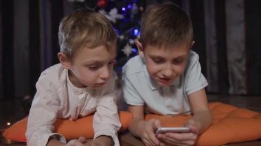 Noel ağacı yakın yerdeki süslü turuncu yastıklar üzerinde iki çocuk yalan