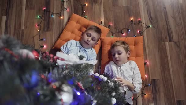 İki güzel çocuk Noel ağacı yakınındaki yastıklar üzerinde mutlu yalan — Stok video