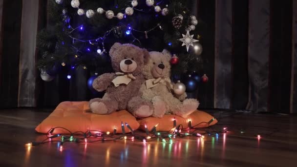 Ездить на фотоаппарате на двух игрушечных плюшевых мишках, сидящих на апельсиновых подушках рядом с елкой. Рождественский декор, квартира, мягкие игрушки, светящиеся гирлянды — стоковое видео