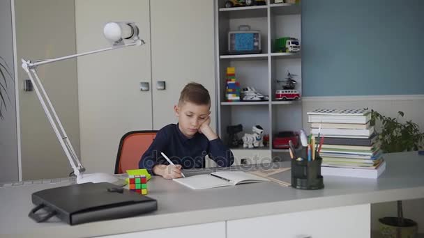 Gyönyörű kisfiú tanul, vagy csinál házi feladatot, iskolás tanul notebook és a könyvek tábla. Aranyos szép diák ő tanulságok otthon — Stock videók