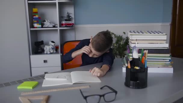 Un niño es un colegial que se despierta en una mesa en la que hace sus deberes. Niño cansado de la tarea. Libros y cuadernos sobre la mesa — Vídeo de stock