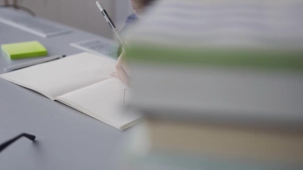 Un grand plan pour un étudiant qui s'assoit à la table et effectue un devoir. Un élève dessine un tableau. Le garçon a une règle, un crayon et un album pour le dessin 