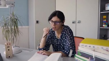 Güzel genç kız masada oturan ve evde kitap okurken gözlük. Ev ödevi