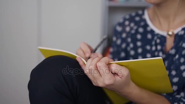 En attraktiv ung kvinna i glas sitter på tabellen arbete på morgonen och gör några anteckningar med en blyertspenna i en anteckningsbok — Stockvideo