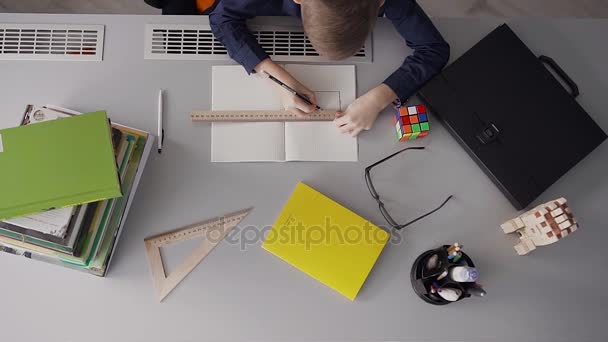 Un pequeño estudiante dibuja un diseño de la casa, cuyo diseño está sobre la mesa. Joven arquitecto — Vídeos de Stock