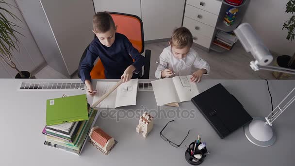 Dois alunos fazem trabalhos de casa em casa. Os rapazes desenham desenhos para casas que estão na mesa. Dois meninos da escola júnior fazendo aulas em casa — Vídeo de Stock