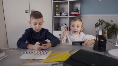 Güzel çocuklar cep telefonları ile eğlenceli oyun bağımlısı yüzler. İki erkek iskambil online spor evde telefon kullanarak masada oturan