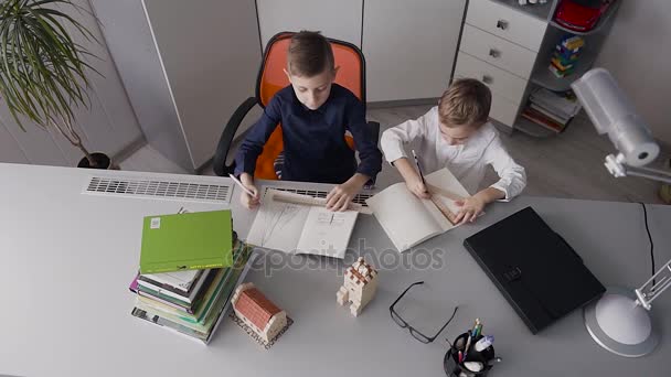 Το Top view. Τα δύο αδέλφια κάθονται στο γραφείο στο σπίτι σε λευκό δωμάτιο και σχεδιάστε σχέδια. Τα παιδιά τελειώσει κάνει δουλειά και διασκέδαση κάθε άλλο χαστούκισε στην παλάμη του τα χέρια τους — Αρχείο Βίντεο