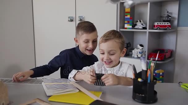 화이트 테이블에 앉아 두 명의 작은 아이 들 룸과 재미를 휴대 전화에서 무선 연결을 통해 무료 인터넷 네트워크를 사용 하 여 — 비디오