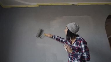 Gri şapkalı bir genç bir kadın bir duvar gri renkli yeni evinde berabere, kulaklık ve dans eğlenceli telefondan müzik dinliyor