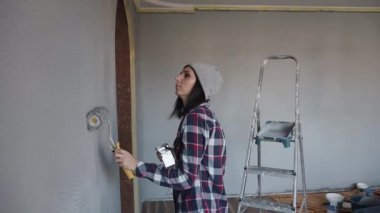 Gri şapkalı bir genç bir kadın bir duvar gri renkli yeni evinde berabere, kulaklık ve dans eğlenceli telefondan müzik dinliyor