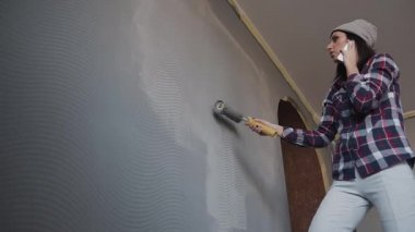 Kız gri odasında duvar boyaları ve telefonla konuşuyor. Dairede onarın. Duvarları yeni bir renkle boyanır. Kadın cep telefonu ve boyama duvar yeni evinde söz