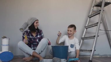 Anne ve oğlu onlar yerde oturur Oda onarım ve birbirlerine boya ile boyama tamamlandı. Bir kadın bir rulo elinde tutar. Mutlu gün - tamamlandı onarım