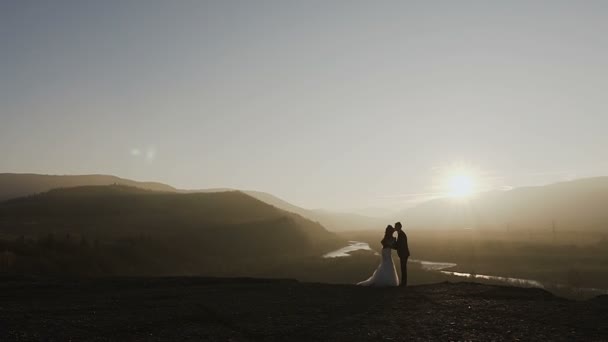 Puesta de sol en las montañas. Hermosa pareja joven abrazándose en la puesta de sol en el fondo del río y el bosque. Concepción del día de la boda — Vídeos de Stock