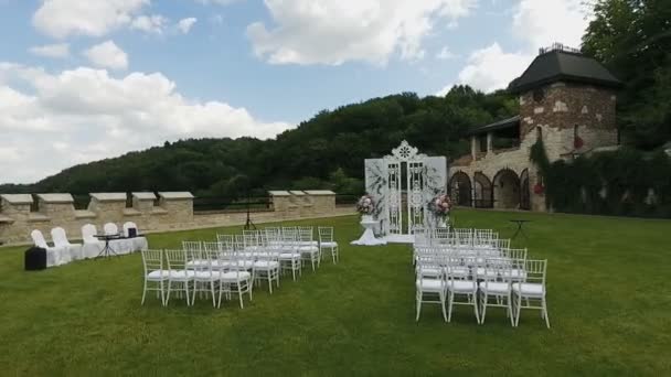Sillas de boda blancas. Boda puesta en el jardín. Filas de sillas vacías de madera blanca en el césped antes de la ceremonia de boda. Día de la boda — Vídeo de stock