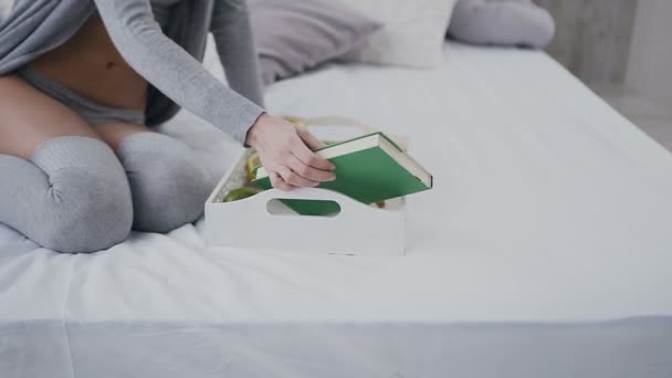 Vacker flicka i glasögon som sitter på sängen med frukost på facket och öppnar bok för läsning. Morgon, utsökt frukost, intressant bok — Stockvideo