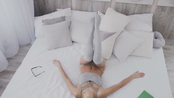 Szczęśliwa młoda kobieta spada na łóżko w sypialni białe. Piękna dziewczyna uśmiechając się, otwiera oczy i patrząc na kamery. Słoneczny poranek czas, biały minimalistyczne wnętrza nowoczesne sypialnia — Wideo stockowe