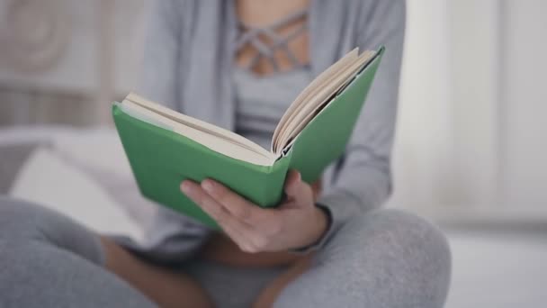 Крупный план Молодая девушка держит в руках книгу, открывает ее и оставляет страницы, чтобы начать читать ее. Красивая девушка в очках открывает книгу — стоковое видео