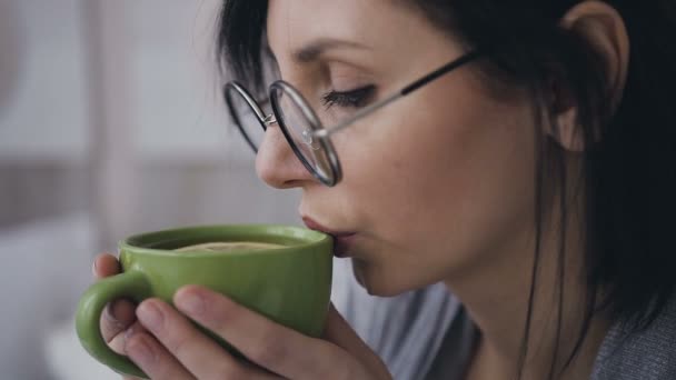 Крупный план лица молодой девушки в очках для изображения, она пьет горячий чай с лимоном — стоковое видео