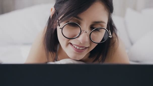 Μελαχρινή νεαρή γυναίκα στο μάτι γυαλιά μόδας ψάχνει οθόνη, σερφάρισμα στο διαδίκτυο. Κομψό μελαχρινή εργασίας με φορητό υπολογιστή και χαμογελαστός από το σπίτι της στο γραφείο στο σπίτι — Αρχείο Βίντεο