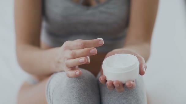 Uma jovem aplica um creme corporal na perna. Uma mulher segura um frasco de hidratante nas mãos e aplica creme nas pernas com um toque nas mãos. Cuidados corporais — Vídeo de Stock