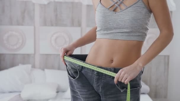 Närbild en kvinna med en sport figur mäter storleken på hennes byxor efter bantning. vacker kropp och platt mage. — Stockvideo