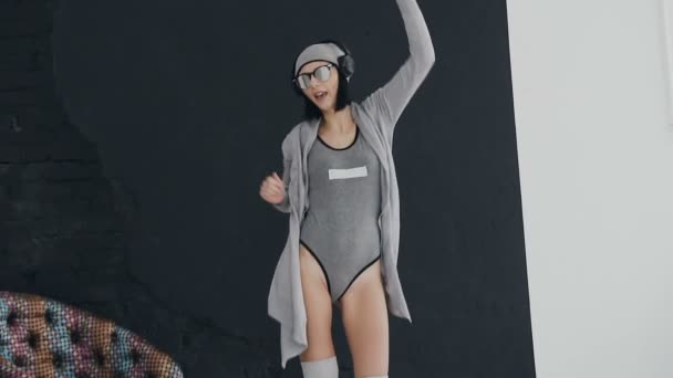 Hipster meisje luistert naar muziek in haar hoofdtelefoons en dansen tegen de achtergrond van een zwart-witte muur — Stockvideo
