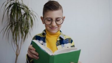 Evde beyaz duvarının yakınında katta otururken bir kitap okumak güzel küçük öğrenci bardaklarda yakın-up. Kapalı. Portre
