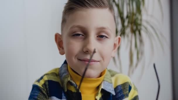 Close-up. The cute face of charming boy schoolboy with beautiful blue eyes who looks at the camera and wears glasses. In the white background, indoors — Stock Video