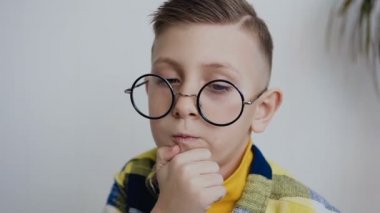 Etkileyici küçük 7-8 yaş çocuk ile güzel bir gülümseme ve mavi gözler gözlük ile ilginç bir fikir hakkında düşünme yan yolları ile acımak yüz arar ve sakalını elini tutar