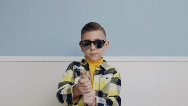 El chico dispara caramelos y petardo. joven con gafas negras sobre el fondo de una pared blanca — Vídeos de Stock