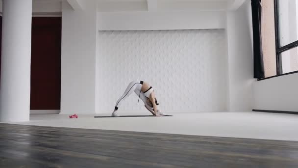 Mujer joven estirando sus piernas en yoga de pie ejercicio de estiramiento como parte de una rutina de fitness o estilo de vida activo. Chica fitness haciendo calentamiento antes del entrenamiento haciendo dedo del pie pierna tacto se estira en el interior en — Vídeo de stock
