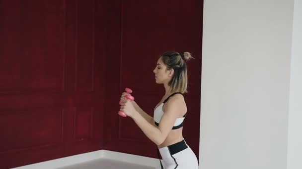 Genç ve atletik kız ya da kadın kolları, el, atlet yükseltir kaslarını güçlendirmek için dumbbells ile egzersizleri yapıyor rüzgarlar onu geri fitness kulübünde — Stok video