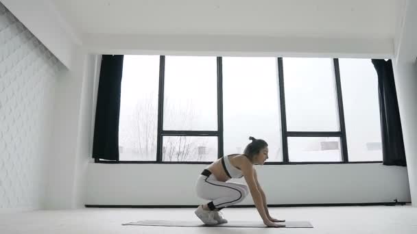 Jóvenes ejercicios de fitness mujer rubia en el gimnasio cerca de grandes ventanas durante el deporte de la mañana, entrenamiento. Ella se vistió con ropa deportiva blanca — Vídeos de Stock