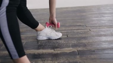 İleri bükme. Hiç bir şey yapıyor ve dumbell dururken spor salonunda tutan spor genç güzel sarışın kadın yan görünüm