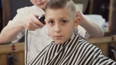 Hoş çocuk bir berber göz fotoğraf makinesine bir sandalyeye oturur ve her şey yolunda ve onun Kuaför ve yeni saç modeli hoşlanıyor eliyle gösterir. Güzel saç. Çocuğu erkek Kuaför