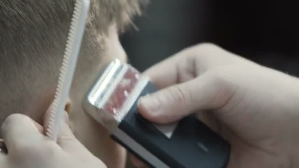 Barber making haircut with trimmer. A cute little boy gets his haircut at skill based barber shop with close up of electric trimmer against his head — Stock Video