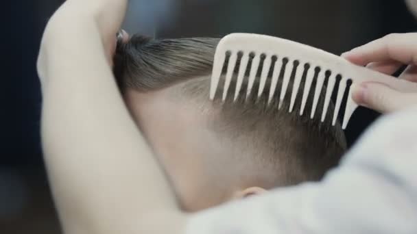 Kapper zet haar naar zijn kleine client. De jongen heeft een nieuw kapsel. Baby kapsel in de barbershop — Stockvideo