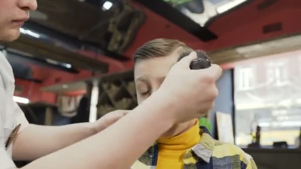The boys face in who a new stylish haircut. The barber makes a hairstyle for a little boy in a male barbershop. Barber dois hairstyle to little boy in barbershop — Stock Video